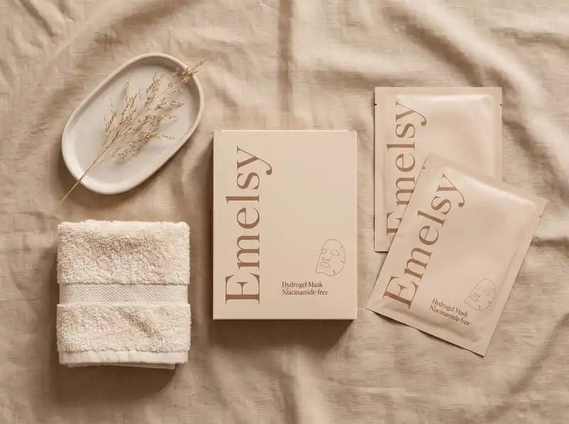 Emelsy box and sachets on beige linen beside a folded towel